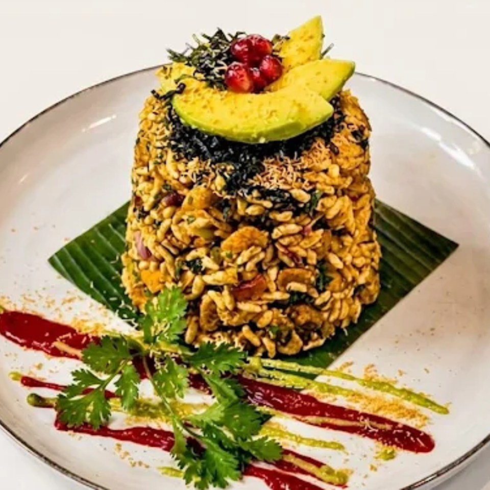 Tower of seasoned rice and grains topped with avocado and berries, garnished with cilantro and colorful sauces on a plate.