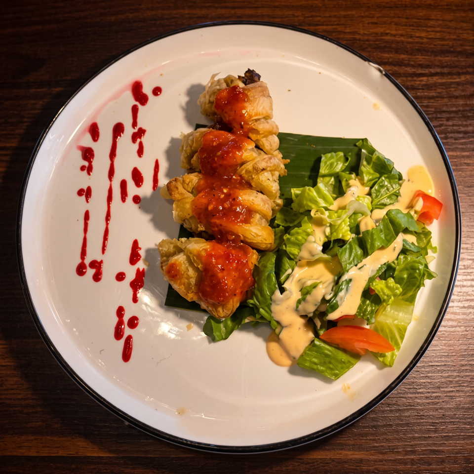 Crispy stuffed rolls topped with red sauce, served beside dressed green salad and decorative sauce drizzles on a white plate.